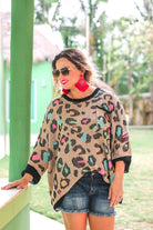 three quarter cuffed sleeve sweater made from unlined loose knit material with a rounded neckline, a chest pocket, and an oversized fit on a multicolor leopard pattern (blue, green, pink, and orange), a black accent color (chest pocket trim, cuffs, and hem), and a brown base