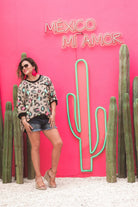 three quarter cuffed sleeve sweater made from unlined loose knit material with a rounded neckline, a chest pocket, and an oversized fit on a multicolor leopard pattern (blue, green, pink, and orange), a black accent color (chest pocket trim, cuffs, and hem), and a brown base