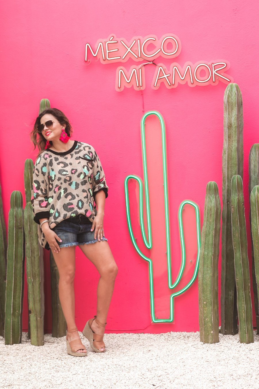 three quarter cuffed sleeve sweater made from unlined loose knit material with a rounded neckline, a chest pocket, and an oversized fit on a multicolor leopard pattern (blue, green, pink, and orange), a black accent color (chest pocket trim, cuffs, and hem), and a brown base