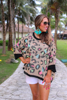 three quarter cuffed sleeve sweater made from unlined loose knit material with a rounded neckline, a chest pocket, and an oversized fit on a multicolor leopard pattern (blue, green, pink, and orange), a black accent color (chest pocket trim, cuffs, and hem), and a brown base