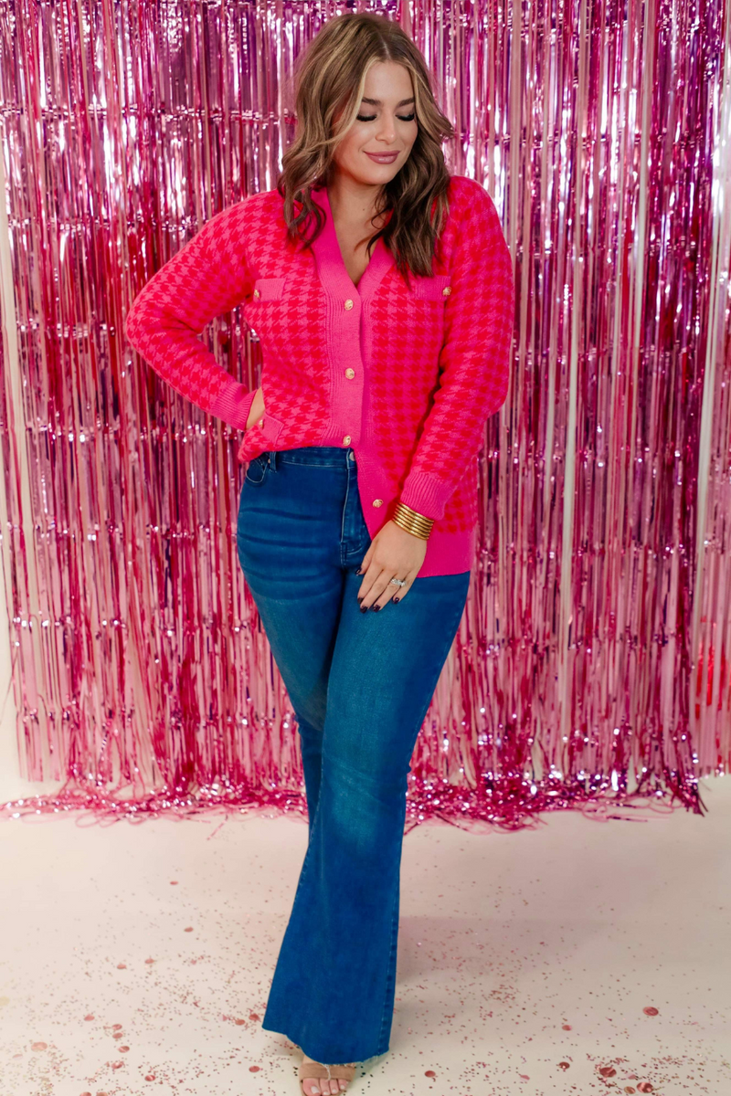 a long-sleeve jacket in a bold pink and red houndstooth pattern with gold detailed buttons, four imitation front pockets, and ribbed classic V-neckline, cuffs, and hemline