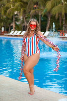 a white one-piece swimsuit made of stretchy material with thick straps, a scoop neckline, a zip front, alternating red and blue vertical stripes, and removable padding