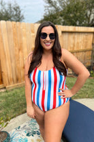 a white one-piece swimsuit made of stretchy material with thick straps, a scoop neckline, a zip front, alternating red and blue vertical stripes, and removable padding