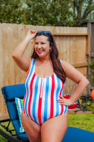 a white one-piece swimsuit made of stretchy material with thick straps, a scoop neckline, a zip front, alternating red and blue vertical stripes, and removable padding