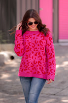 a fuzzy textured long-sleeve sweater with a vibrant pink leopard pattern on a pink base and ribbed detailing on the round neckline, cuffs, and structured hemline