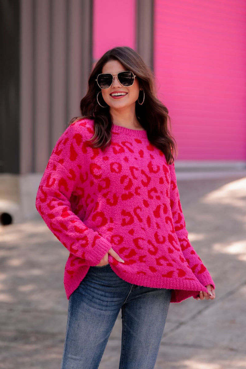 a fuzzy textured long-sleeve sweater with a vibrant pink leopard pattern on a pink base and ribbed detailing on the round neckline, cuffs, and structured hemline