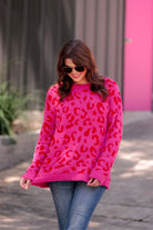 a fuzzy textured long-sleeve sweater with a vibrant pink leopard pattern on a pink base and ribbed detailing on the round neckline, cuffs, and structured hemline