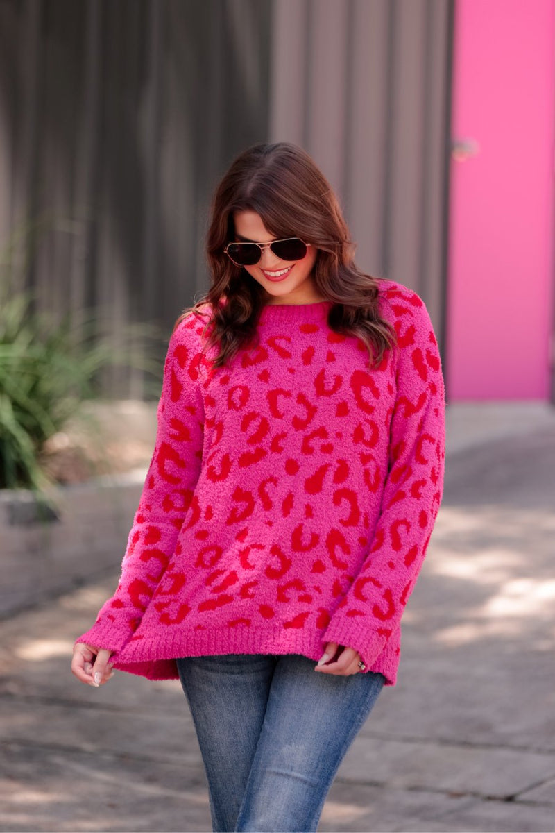 a fuzzy textured long-sleeve sweater with a vibrant pink leopard pattern on a pink base and ribbed detailing on the round neckline, cuffs, and structured hemline