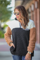 a long-sleeve fluffy pullover with a quarter-leopard snap closure, a faux leopard front chest pocket, a foldable collar, and convenient side pockets on a black, taupe, and white color block fabric that is slightly oversized