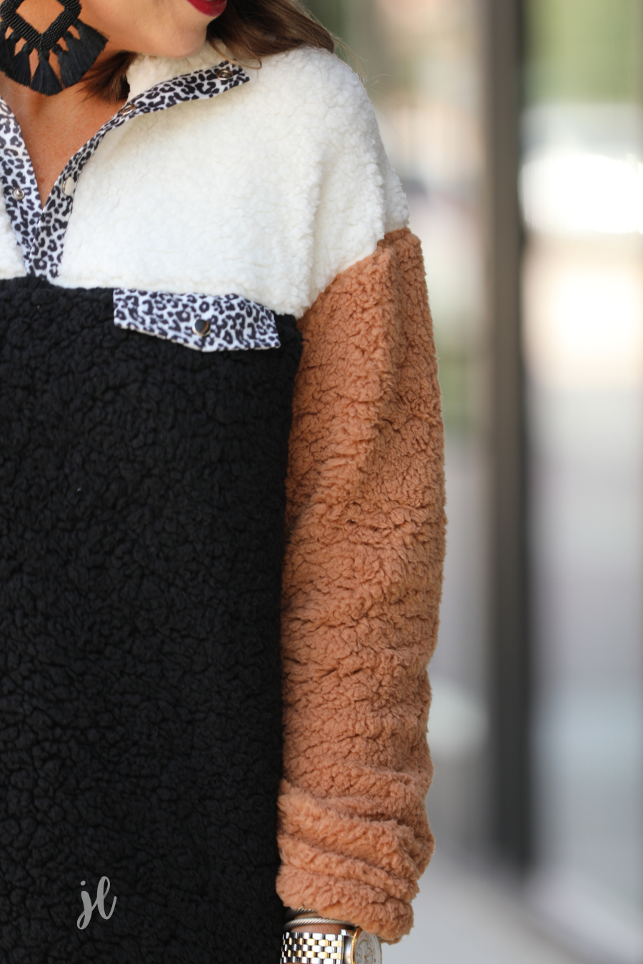 a long-sleeve fluffy pullover with a quarter-leopard snap closure, a faux leopard front chest pocket, a foldable collar, and convenient side pockets on a black, taupe, and white color block fabric that is slightly oversized