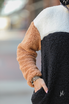 a long-sleeve fluffy pullover with a quarter-leopard snap closure, a faux leopard front chest pocket, a foldable collar, and convenient side pockets on a black, taupe, and white color block fabric that is slightly oversized