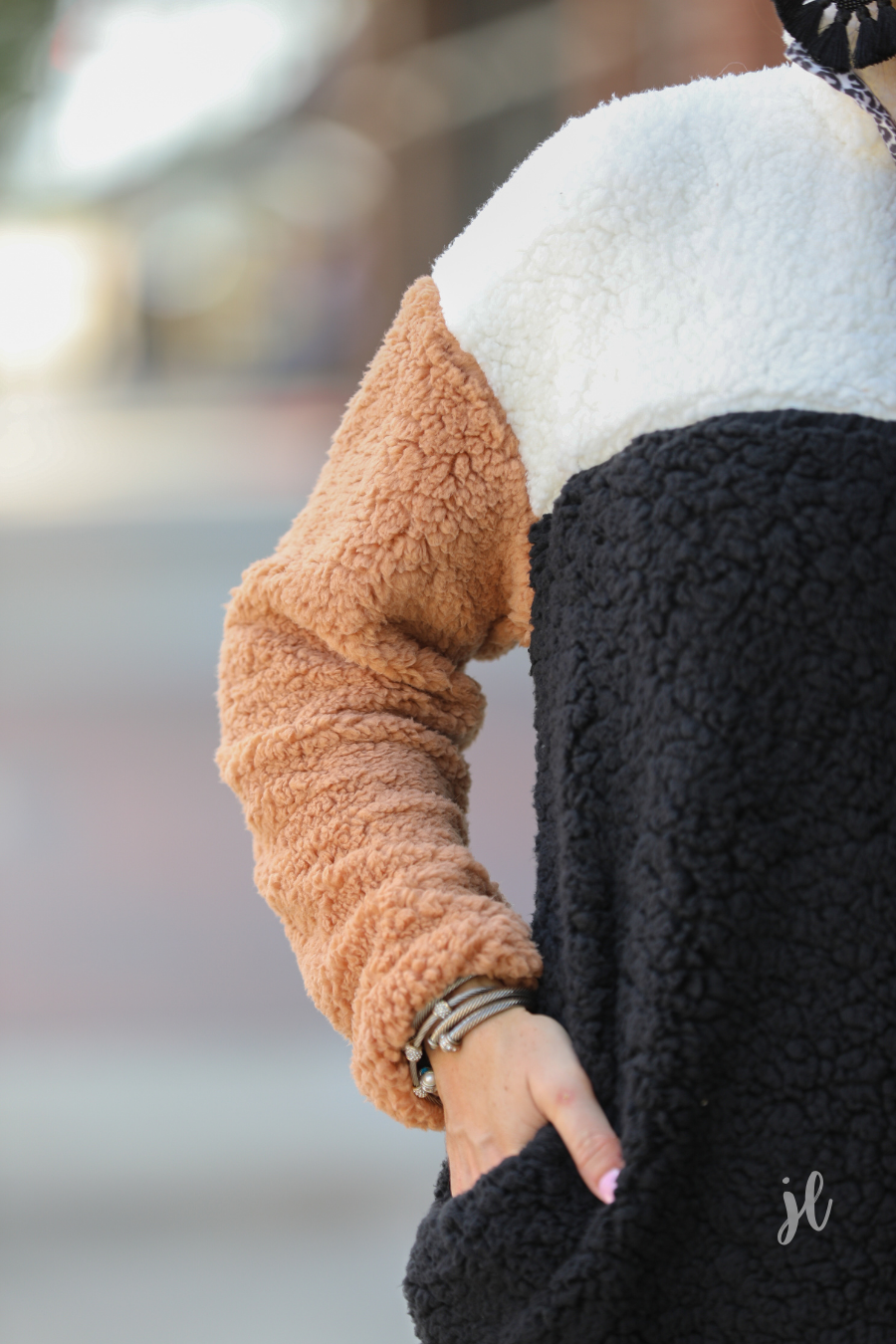 a long-sleeve fluffy pullover with a quarter-leopard snap closure, a faux leopard front chest pocket, a foldable collar, and convenient side pockets on a black, taupe, and white color block fabric that is slightly oversized