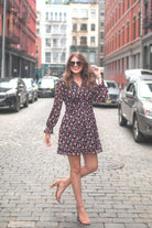 a black floral pattern print dress with sheer long sleeves, smocked cuffs, a ruffle v-neckline, back zipper, tiered ruffle hemline, and full lining with no stretch