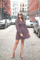 a black floral pattern print dress with sheer long sleeves, smocked cuffs, a ruffle v-neckline, back zipper, tiered ruffle hemline, and full lining with no stretch