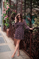 a black floral pattern print dress with sheer long sleeves, smocked cuffs, a ruffle v-neckline, back zipper, tiered ruffle hemline, and full lining with no stretch