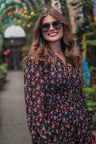 a black floral pattern print dress with sheer long sleeves, smocked cuffs, a ruffle v-neckline, back zipper, tiered ruffle hemline, and full lining with no stretch