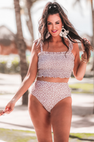 two-piece swimsuit sold separately made of stretchy material with a ruched crop top, adjustable tie straps, and removable padding paired with high-waisted bottoms on a neutral leopard print fabric