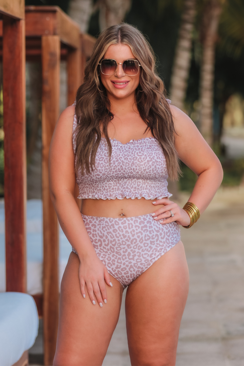 two-piece swimsuit sold separately made of stretchy material with a ruched crop top, adjustable tie straps, and removable padding paired with high-waisted bottoms on a neutral leopard print fabric