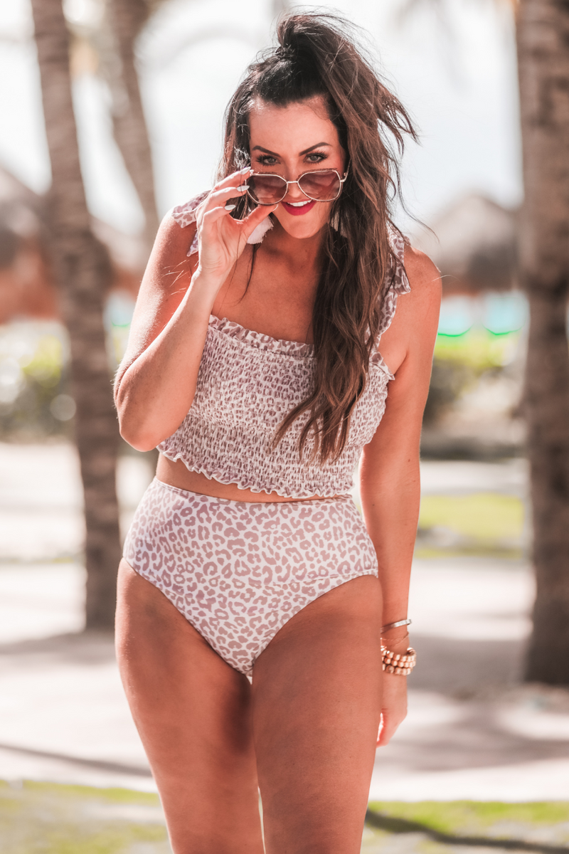 two-piece swimsuit sold separately made of stretchy material with a ruched crop top, adjustable tie straps, and removable padding paired with high-waisted bottoms on a neutral leopard print fabric
