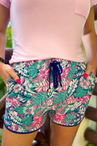mid-rise relaxed fit activewear shorts with side pockets and a tie waist drawstring with gold bead accents, designed on a colorful palm leaves pattern print fabric, hot pink base, and royal blue trim