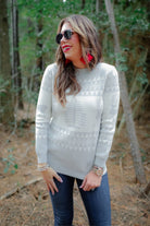 a grey long-sleeve heavy sweater with a ribbed detailing on the neckline, cuffs, and hem on a festive grey and white holiday pattern fabric