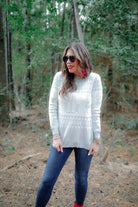 a grey long-sleeve heavy sweater with a ribbed detailing on the neckline, cuffs, and hem on a festive grey and white holiday pattern fabric