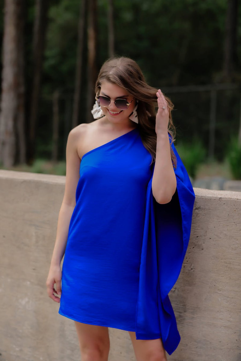 a royal blue one-shoulder mini dress with an asymmetrical neckline and a draping, billowy body creating a relaxed silhouette 