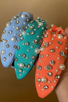 a twisted center knot headband with varying sizes of pearl and rhinestone detailing in blue, coral, and teal