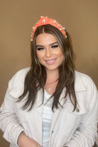 a twisted center knot headband with varying sizes of pearl and rhinestone detailing in coral