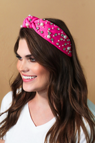 a twisted center knot headband with varying sizes of pearl and rhinestone detailing in pink