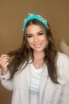 a twisted center knot headband with varying sizes of pearl and rhinestone detailing in teal