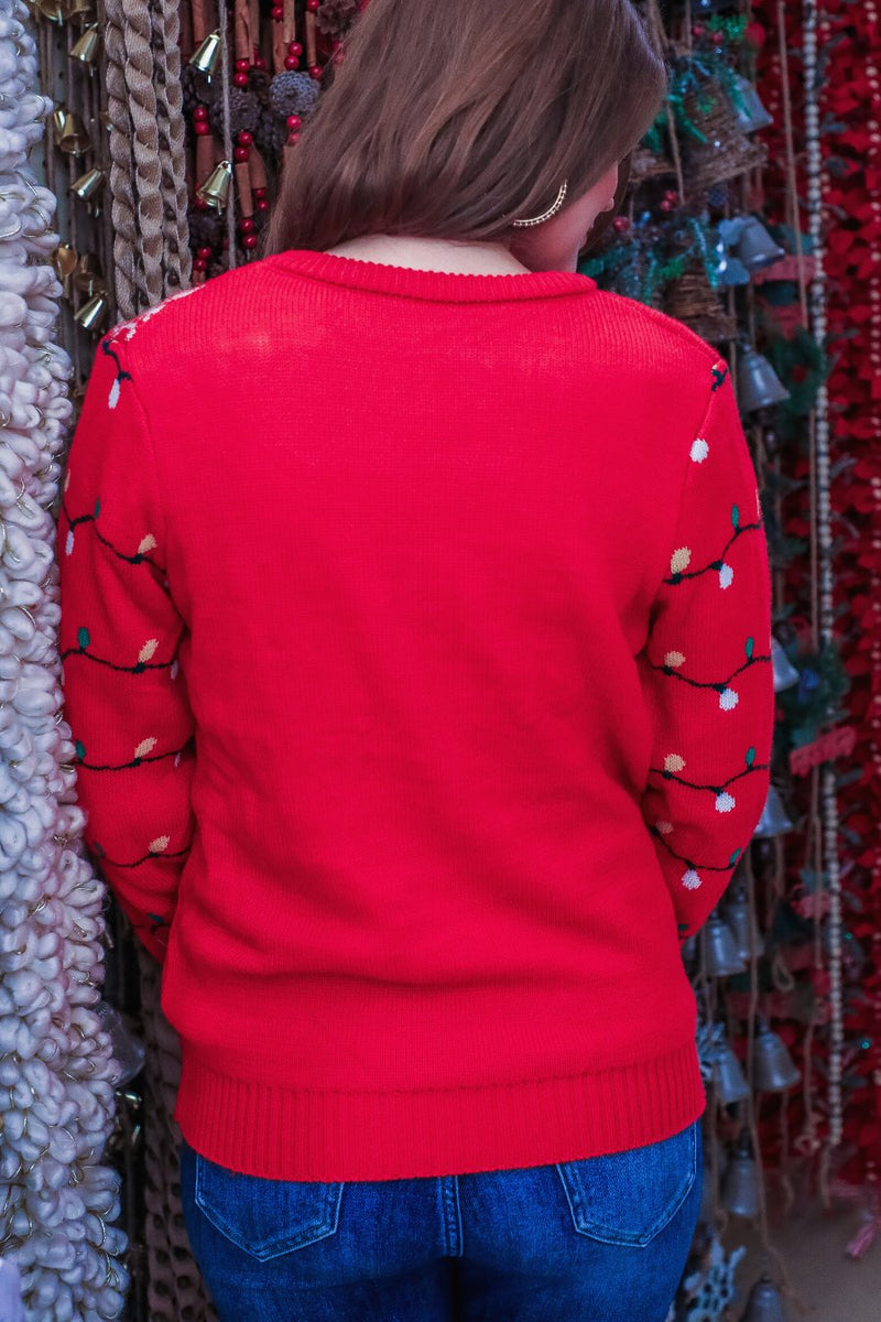 a red long-sleeve heavy sweater made of soft, cozy material with a cheerful reindeer graphic framed by delicate snowflakes, playful snowflake accents, and whimsical multicolor light strands wrapping around the sleeves