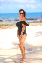 solid black one-piece swimsuit made of stretchy material, a ruffled neckline and straps that can be worn on or off the shoulder, adjustable and removable spaghetti straps, an adjustable crisscrossed cutout back, side ruched detailing, and removable padding