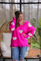 an oversized distressed v-neck long-sleeve sweater with a white heart pattern on a pink knit fabric 