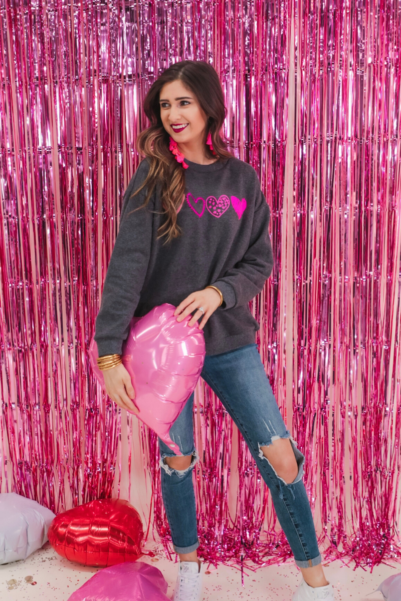 a charcoal long-sleeve sweatshirt with a fuzzy inside, sewn-on pink chenille heart patches, a relaxed drop-shoulder fit, and ribbed detailing on the classic crew neckline, cuffs, and hemline