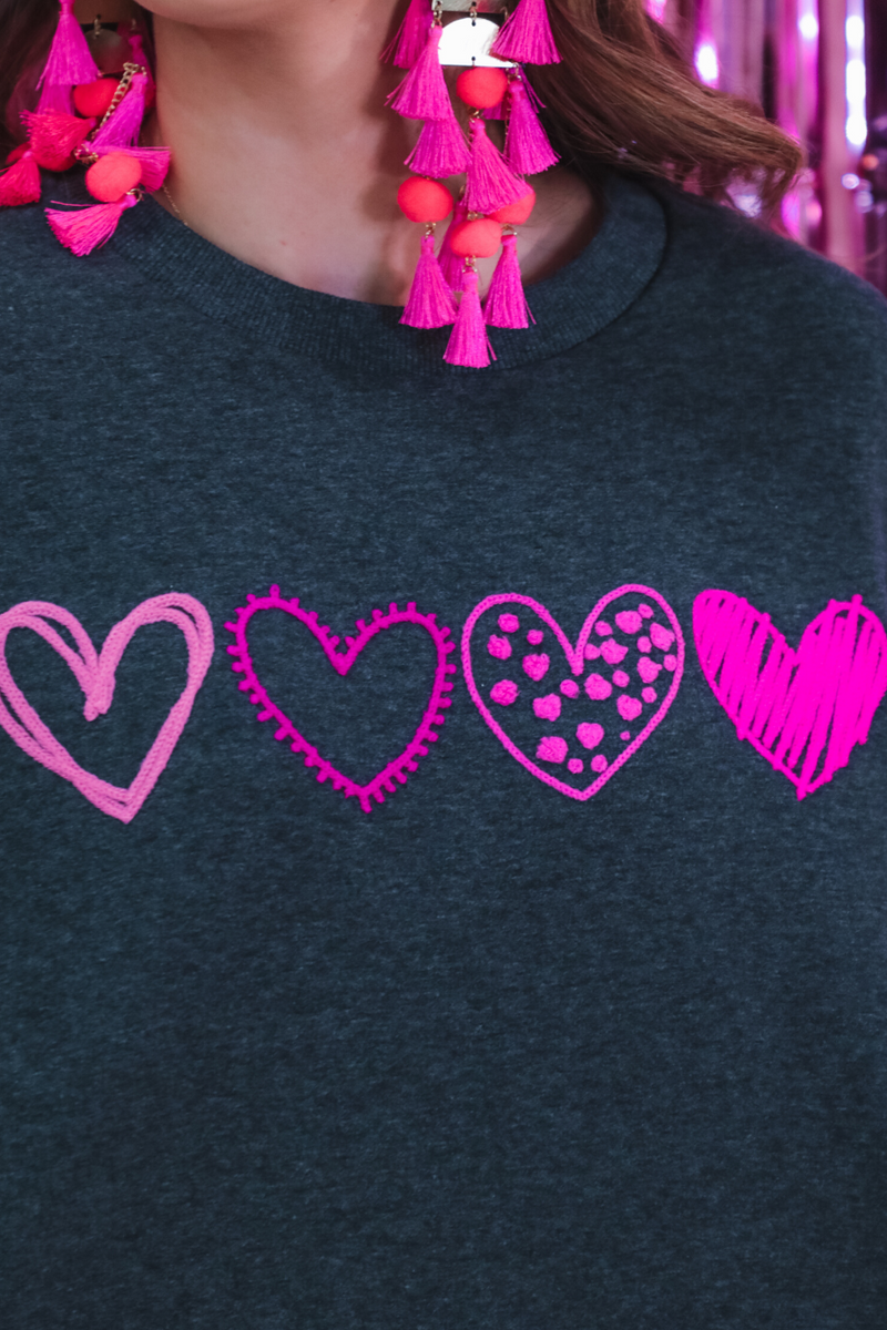 a charcoal long-sleeve sweatshirt with a fuzzy inside, sewn-on pink chenille heart patches, a relaxed drop-shoulder fit, and ribbed detailing on the classic crew neckline, cuffs, and hemline