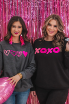 a charcoal long-sleeve sweatshirt with a fuzzy inside, sewn-on pink chenille heart patches, a relaxed drop-shoulder fit, and ribbed detailing on the classic crew neckline, cuffs, and hemline
