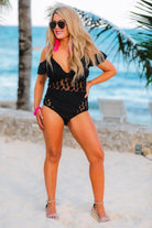 one-piece swimsuit made of stretchy material with a mix of solid black and sheer polka dot fabric, removable padding, ruffle neckline, adjustable spaghetti straps, and chunky shoulder straps that can be worn on or off the shoulder