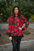 a black long-sleeve tunic with a bold red heart pattern on a black base, side slits, a relaxed drop-shoulder fit, and ribbed detailing on the neckline, cuffs, and hemline