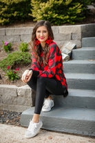 a black long-sleeve tunic with a bold red heart pattern on a black base, side slits, a relaxed drop-shoulder fit, and ribbed detailing on the neckline, cuffs, and hemline
