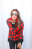 a black long-sleeve tunic with a bold red heart pattern on a black base, side slits, a relaxed drop-shoulder fit, and ribbed detailing on the neckline, cuffs, and hemline