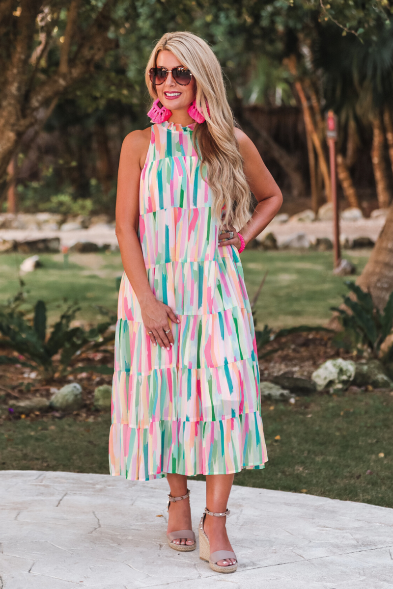 sleeveless dress with a ruffled halter neckline, singular button closure, tiered babydoll style silhouette, and a midi length with lining on a painterly print fabric in multi
