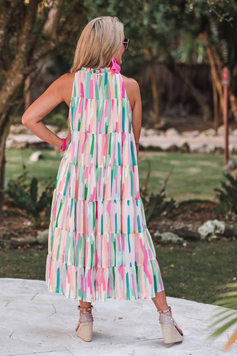 sleeveless dress with a ruffled halter neckline, singular button closure, tiered babydoll style silhouette, and a midi length with lining on a painterly print fabric in multi