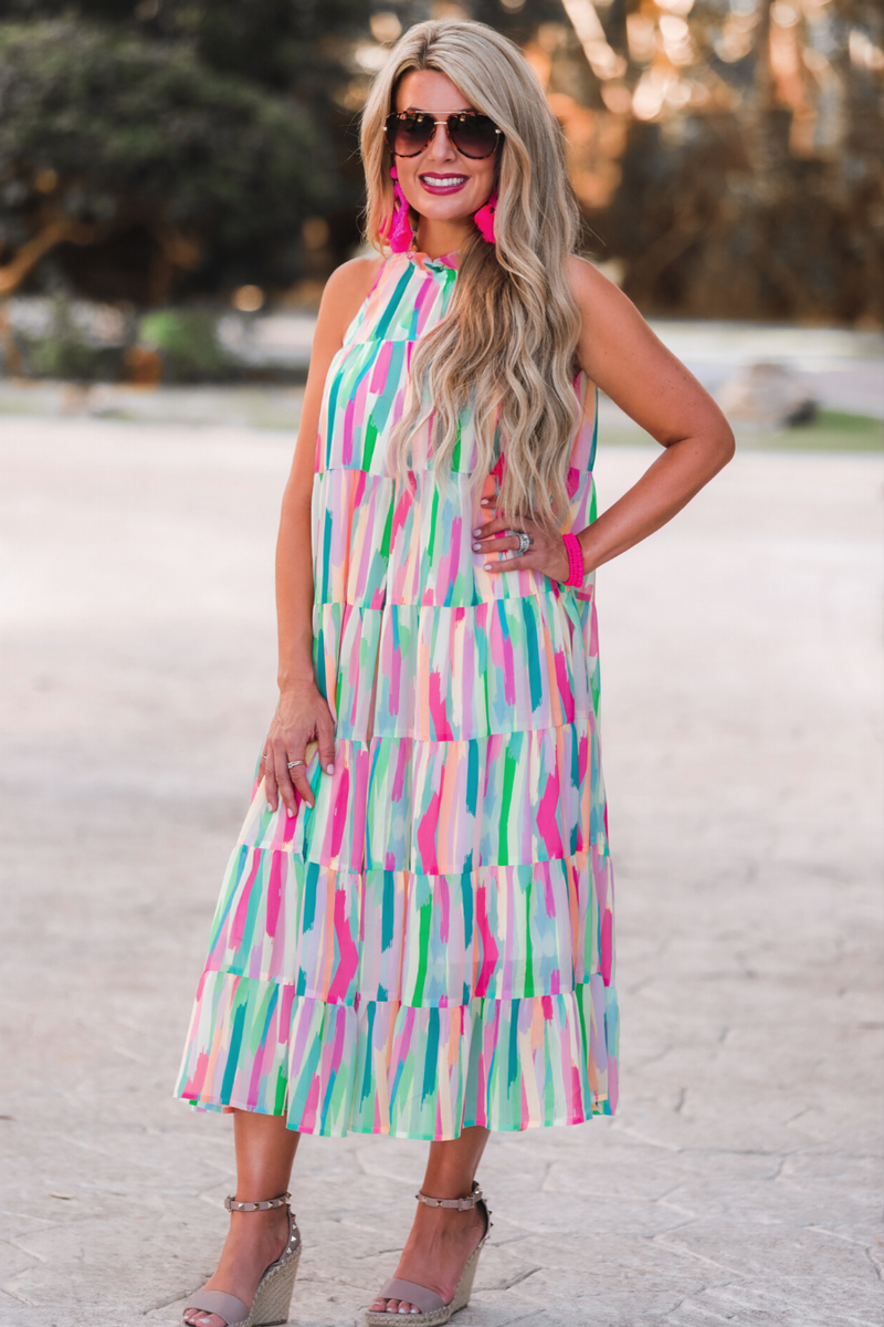 sleeveless dress with a ruffled halter neckline, singular button closure, tiered babydoll style silhouette, and a midi length with lining on a painterly print fabric in multi