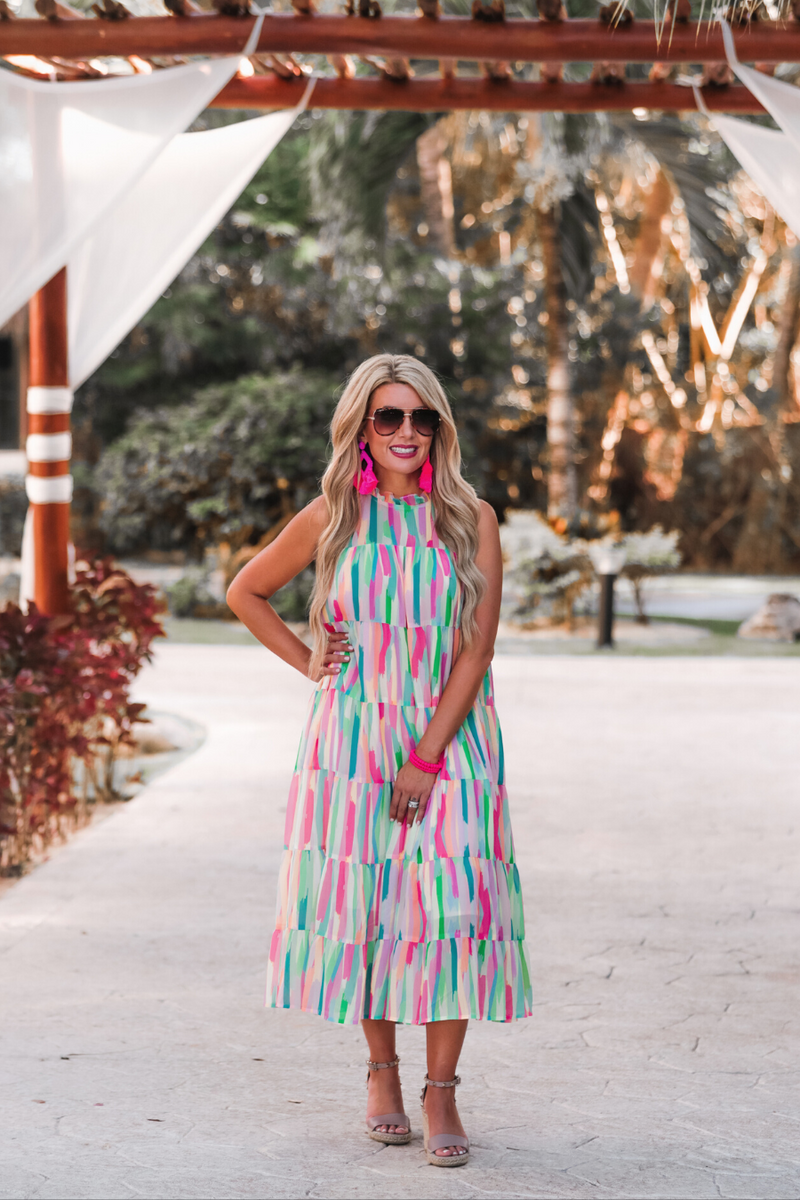 sleeveless dress with a ruffled halter neckline, singular button closure, tiered babydoll style silhouette, and a midi length with lining on a painterly print fabric in multi